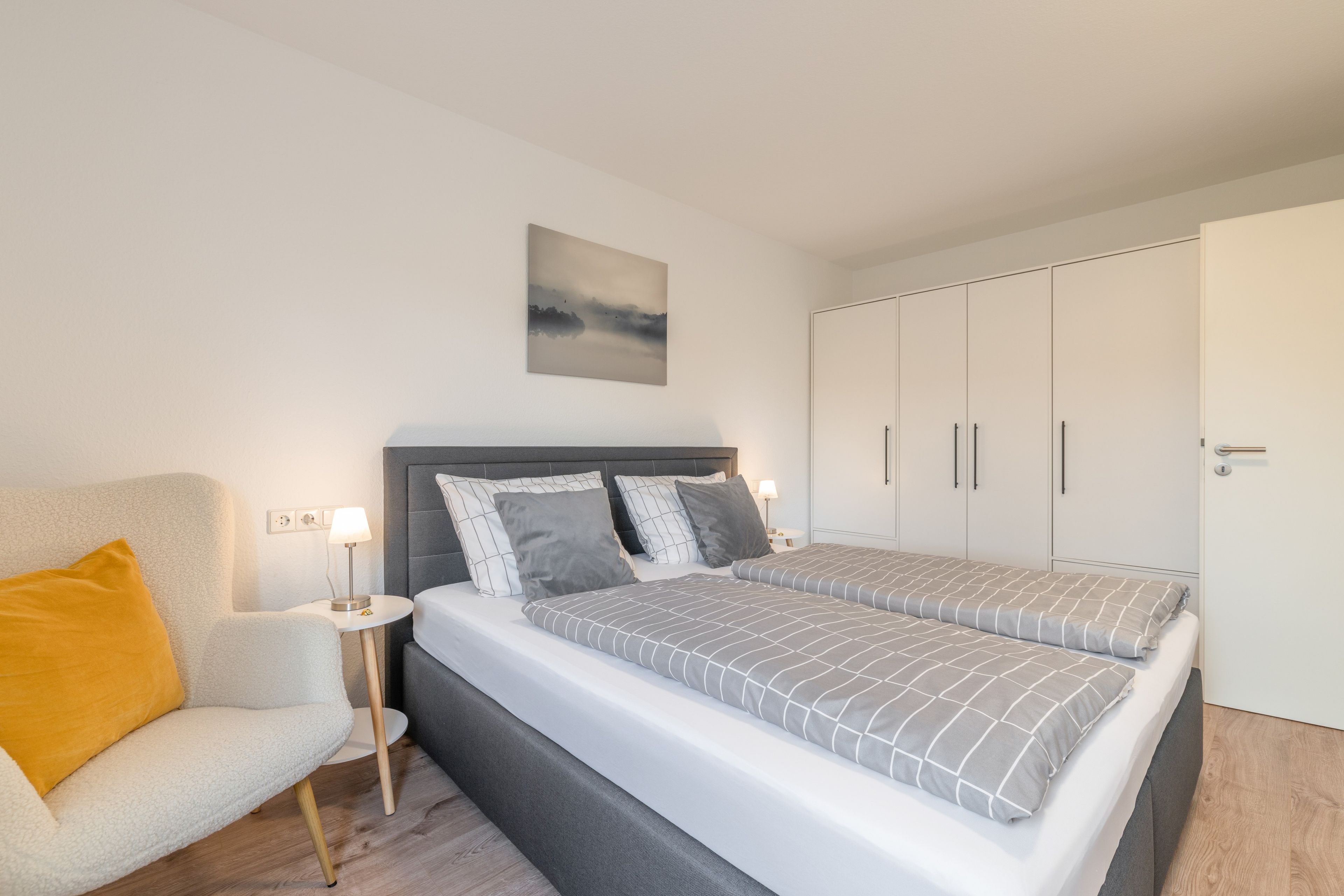 Un dormitorio moderno con cama, una silla, una mesita de noche y un armario.
