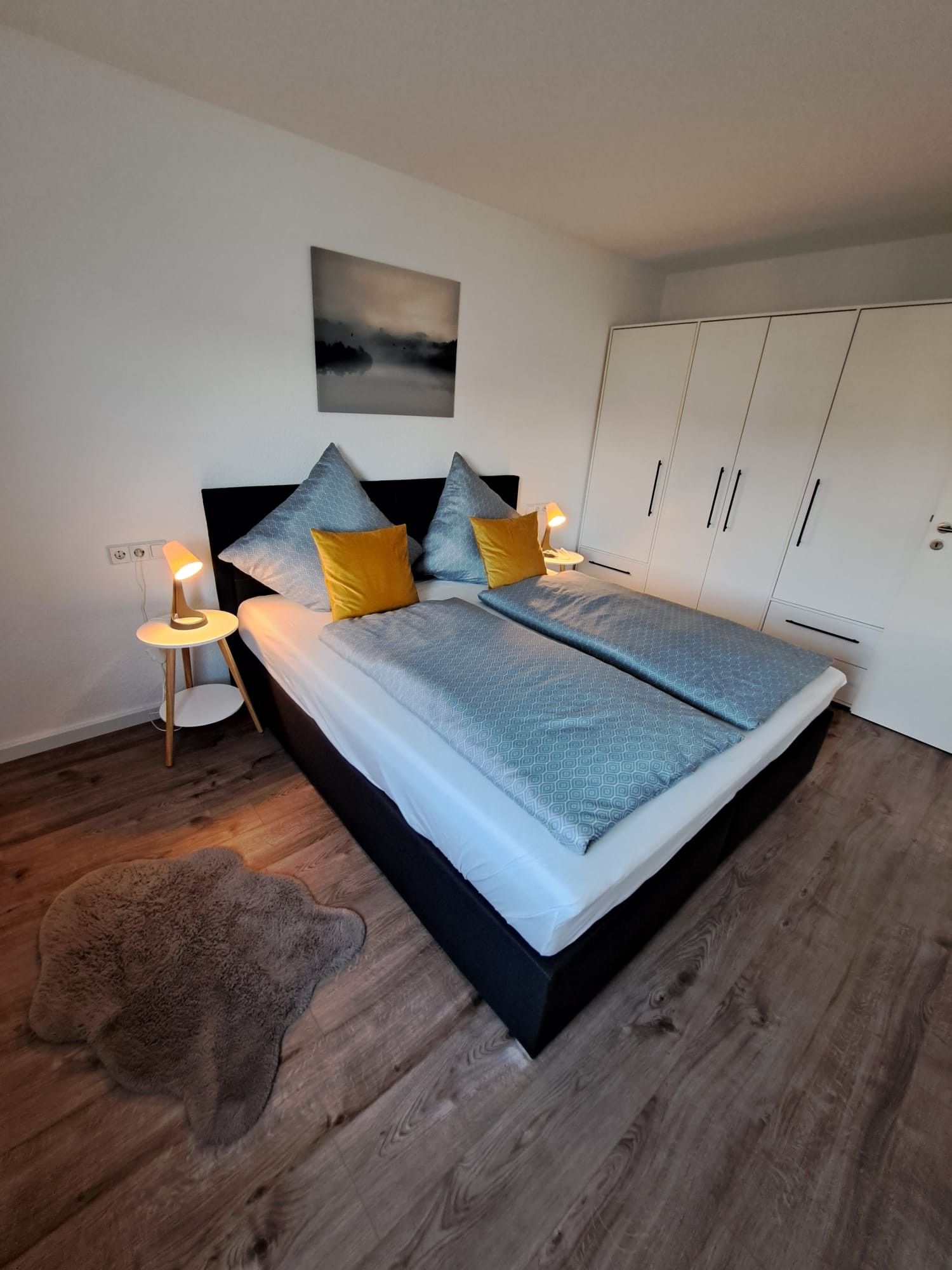 Une chambre à coucher avec un lit, des lampes de chevet, un tableau et une armoire.
