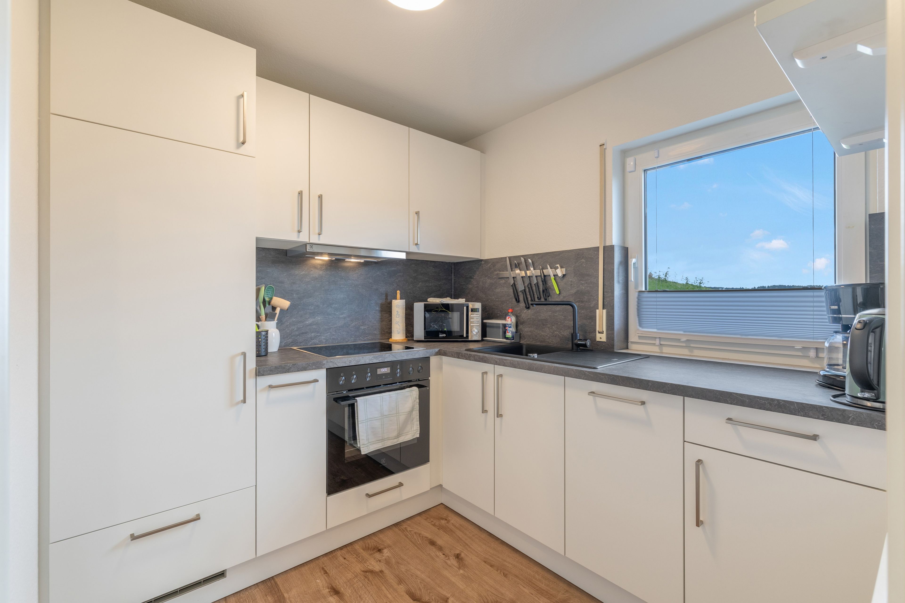 Una cocina moderna con armarios blancos, encimera negra y ventana con vistas al exterior.