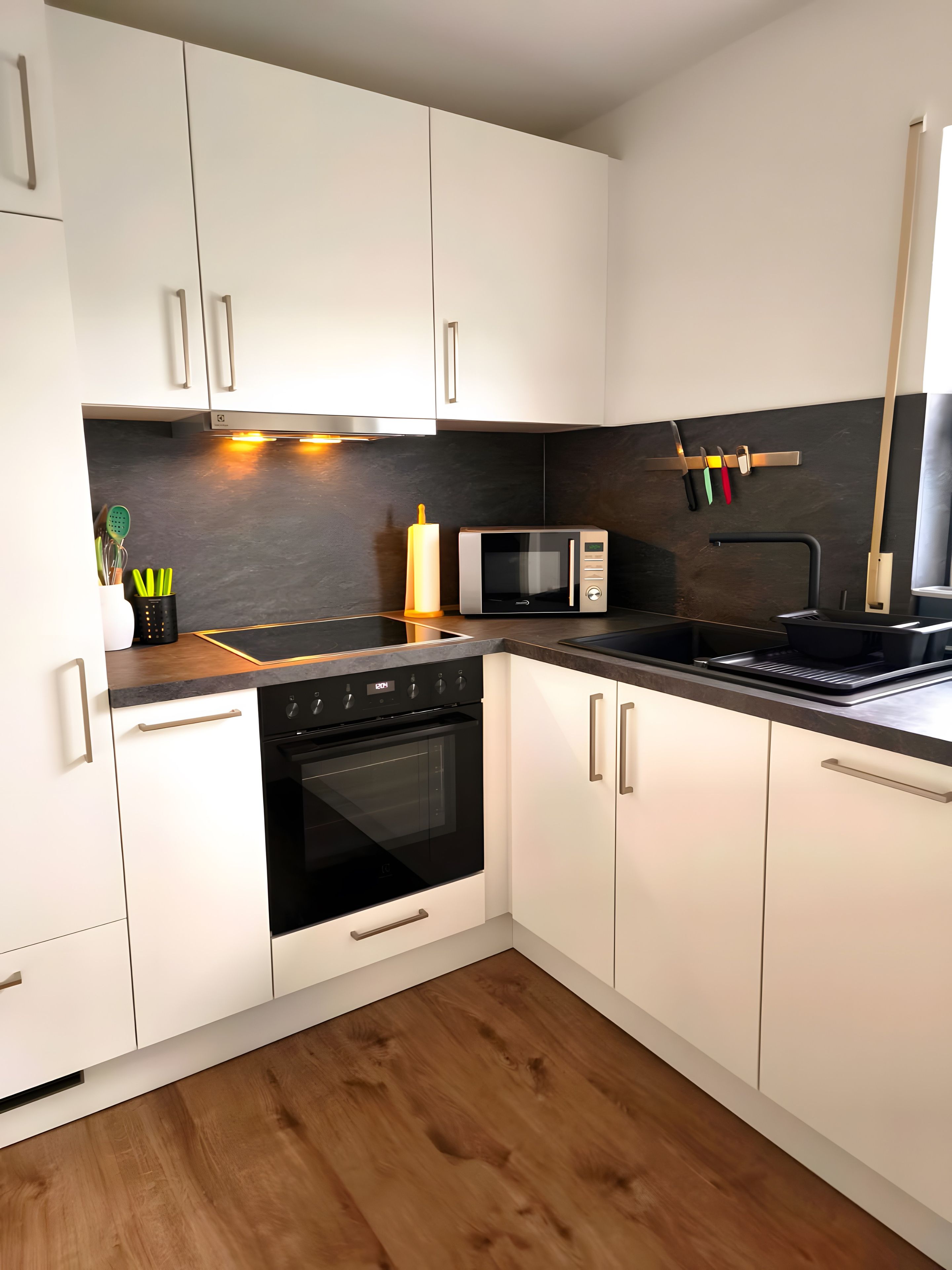 A modern kitchen with white cabinets, a black oven, a microwave, and a wooden countertop.