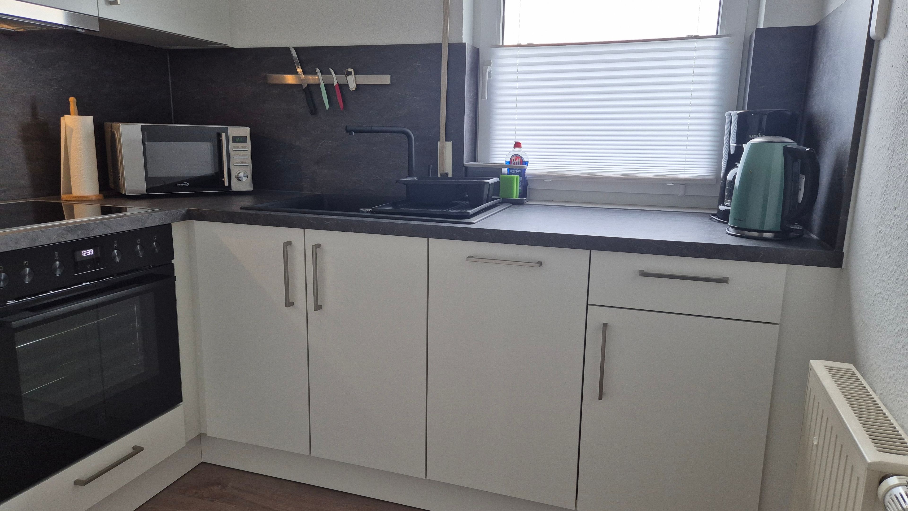 Cocina moderna con microondas, estufa, lavabo y ventana con persianas.
