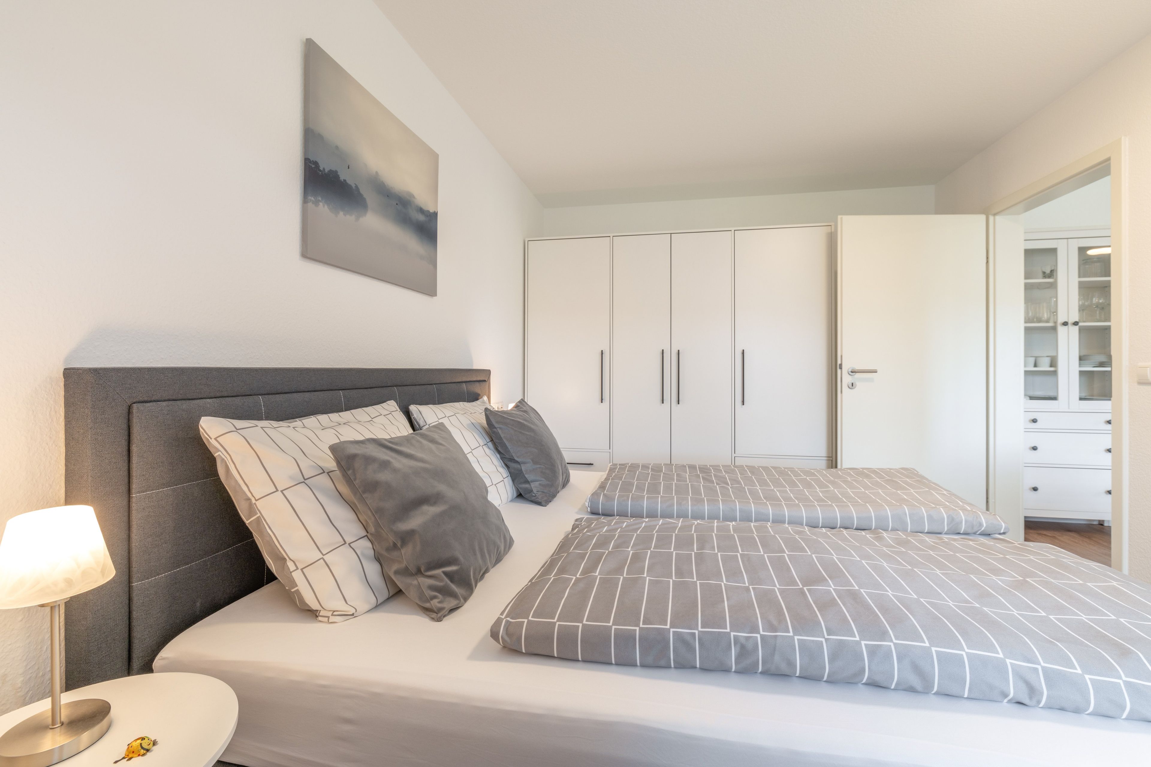 A bedroom with a bed, bedside table, lamp, and a wardrobe.
