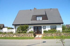 Une maison à deux étages avec un toit sombre, une porte d’entrée et une petite fenêtre.