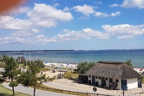Vista costeira com um edifício de telhado de palha, um caminho pavimentado e céu limpo.