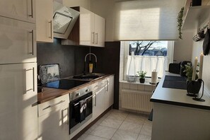 Et moderne køkken med hvide skabe, indbygget ovn, vask og et vindue med udsigt.