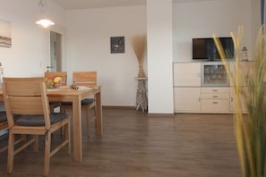 Ein Essbereich mit Holztisch und -stühlen, einer Vase mit Trockenpflanzen und einem Fernseher auf einem Schrank.