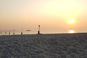 Ein Strand mit Sonnenuntergang, einem Steg und einem Schiff in der Ferne.