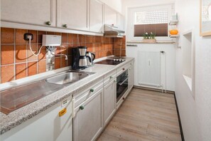 Eine kleine Küche mit Spüle, Herd und Backofen, ausgestattet mit einer Fliesenküchenzeile und Holzböden.