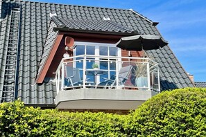 Ein Haus mit geneigtem Dach, einem Balkon mit Stühlen und einem Fenster.