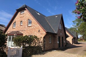 Ein Backsteinhaus mit geneigtem Dach, einer Steinmauer und einem weißen Zaun aus Schindeln.