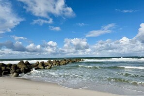 Ein Strand mit einem steinernen Wellenbrecher und Wellen.