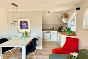 Une cuisine moderne avec des meubles blancs, un coin repas doté d’une table blanche et d’une chaise rouge.