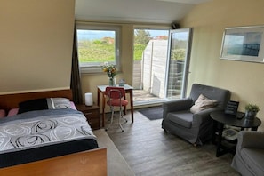 A hotel room with a bed, a desk, a chair, a sofa, and a view through the door. - Holiday apartment in Juist with swimming pool (Juist)