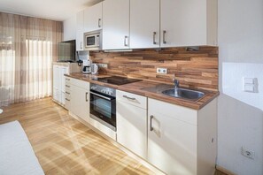 Eine moderne Küche mit weißen Schränken, einer Holzausziehtheke, einer eingebauten Mikrowelle, einem Herd und einem Spülbecken.