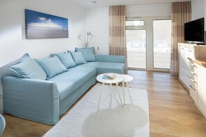Ein modernes Wohnzimmer mit einem hellblauen Sofa, einem kleinen weißen Tisch und einem Fernseher auf einem Schrank.
