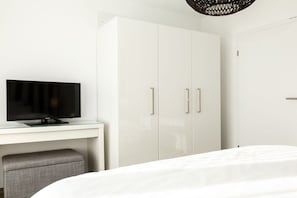 Una habitación de hotel moderna con una cama, un televisor de pantalla plana sobre un escritorio de vidrio y un armario con tiradores plateados.