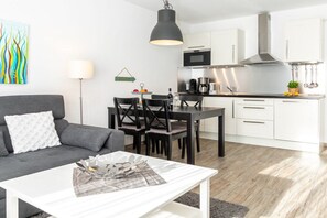 Ein modernes Wohnzimmer mit einer Couch, einem Esstisch mit Stühlen und einer Küchenzeile mit Schränken und Geräten.