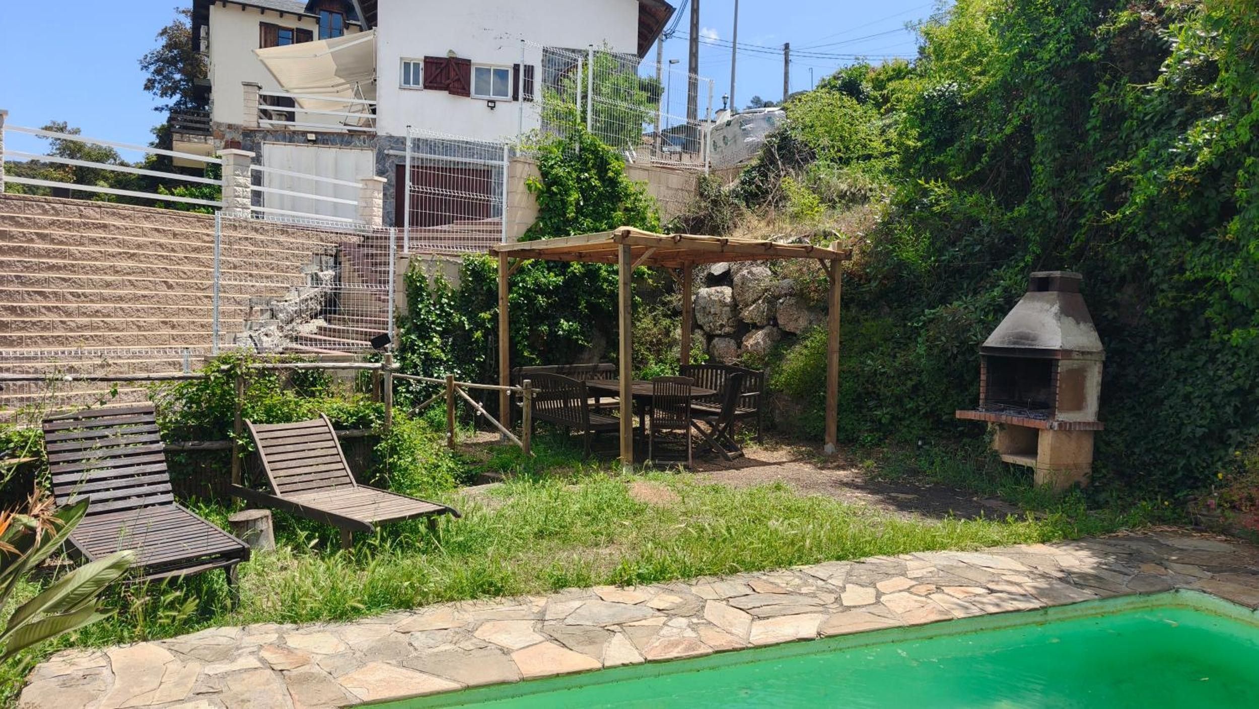 A backyard with a swimming pool, a pergola, outdoor furniture, and a barbecue grill.