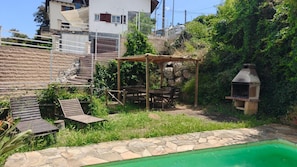 A backyard with a swimming pool, a pergola, outdoor furniture, and a barbecue grill.