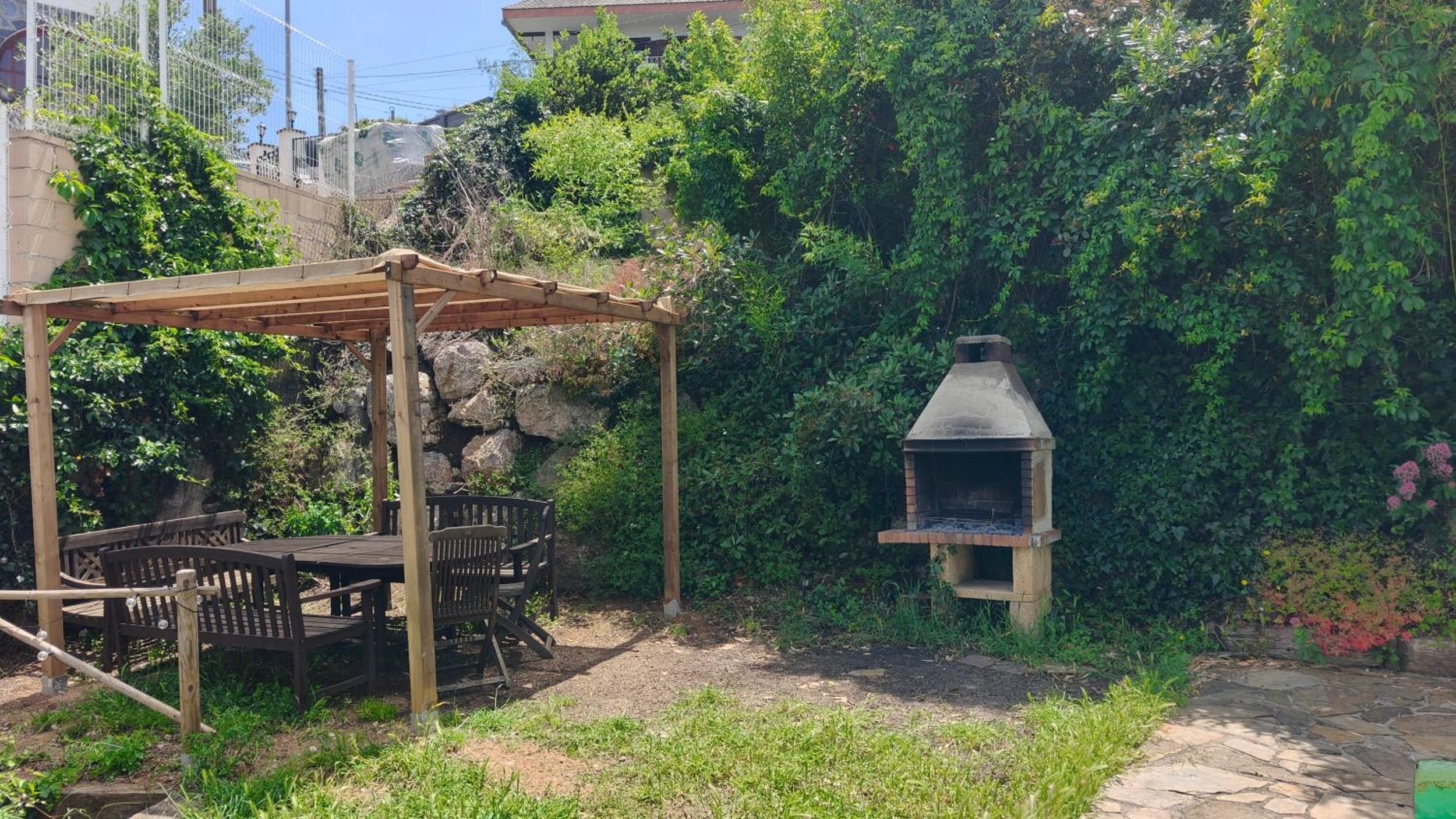 Een terras buiten met een houten tafel en stoelen, een pergola en een pad van stenen.