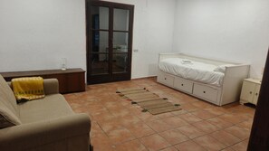 Une petite pièce bien rangée, avec un lit, un canapé, une petite armoire et une porte qui donne sur une autre pièce.