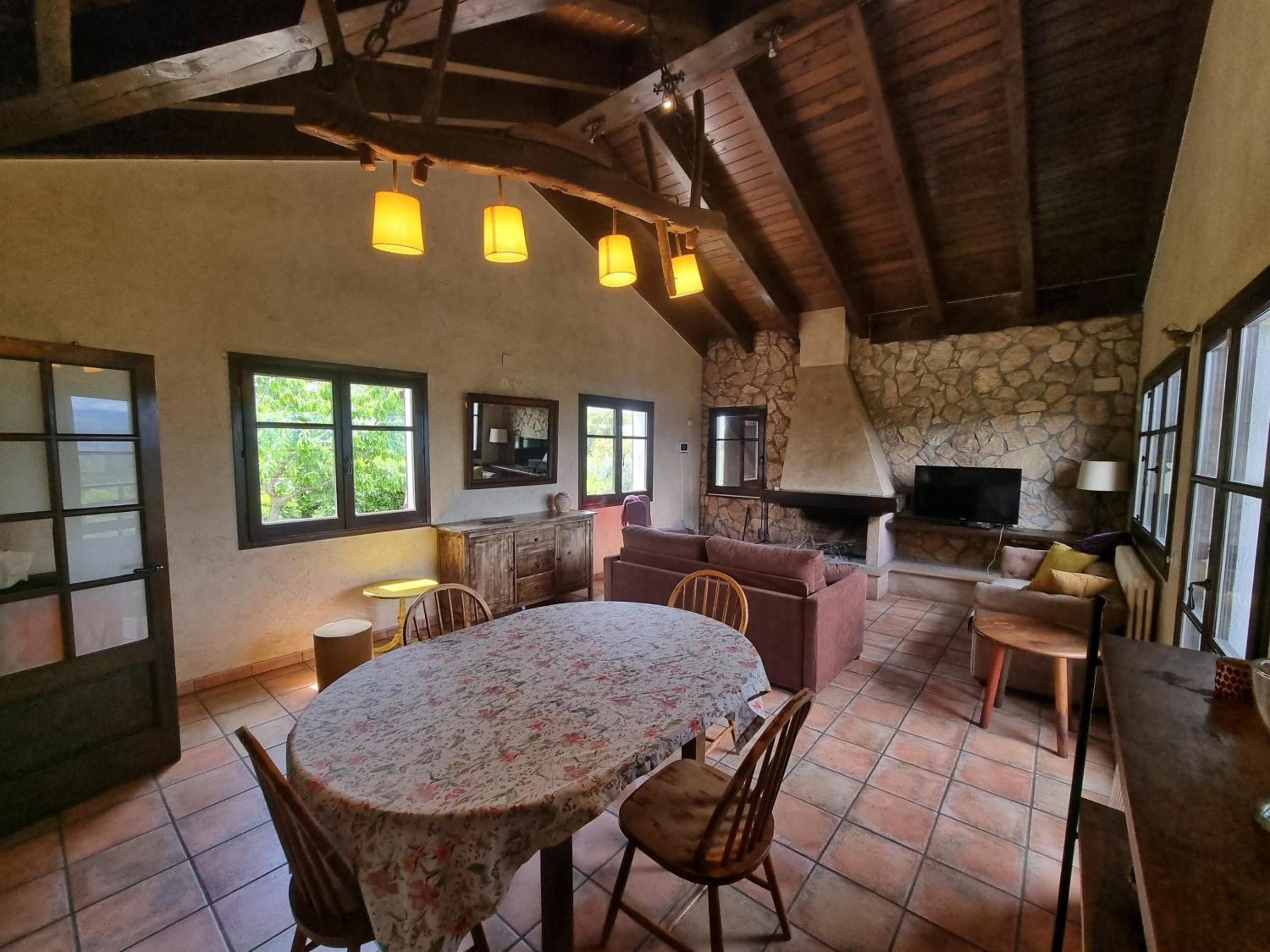 A rustic interior with a stone fireplace, a television, and a dining area with a round table and chairs.
