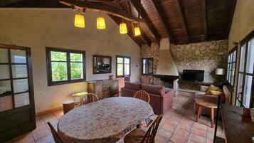 A rustic interior with a stone fireplace, a television, and a dining area with a round table and chairs.