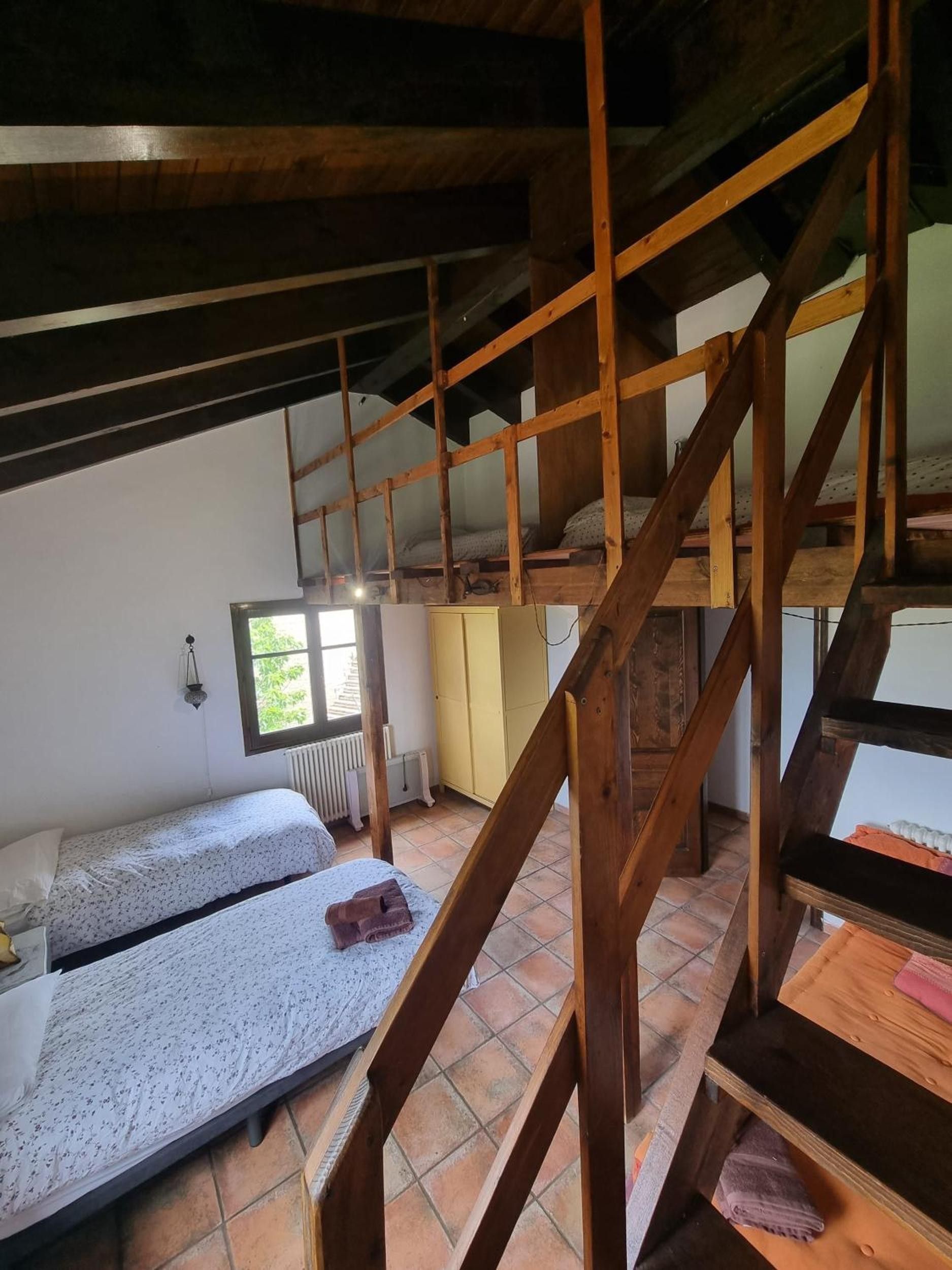 A room with a wooden staircase, two beds, a window, and a radiator.