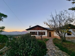 Une maison avec un chemin de pierre menant à l’entrée, entourée de verdure et offrant une vue sur des montagnes lointaines.
