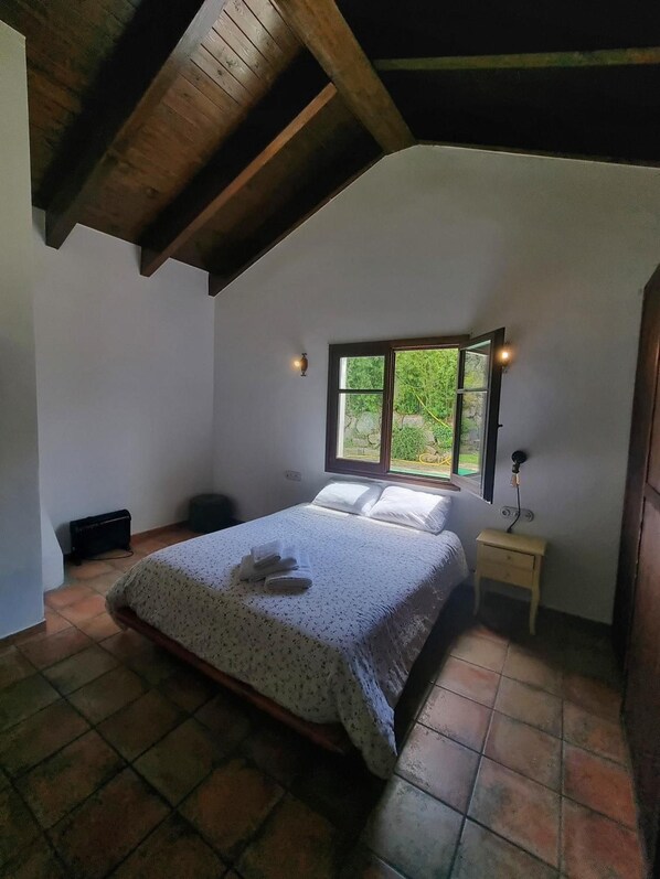 A bedroom with a bed, a nightstand, a window, and a radiator.