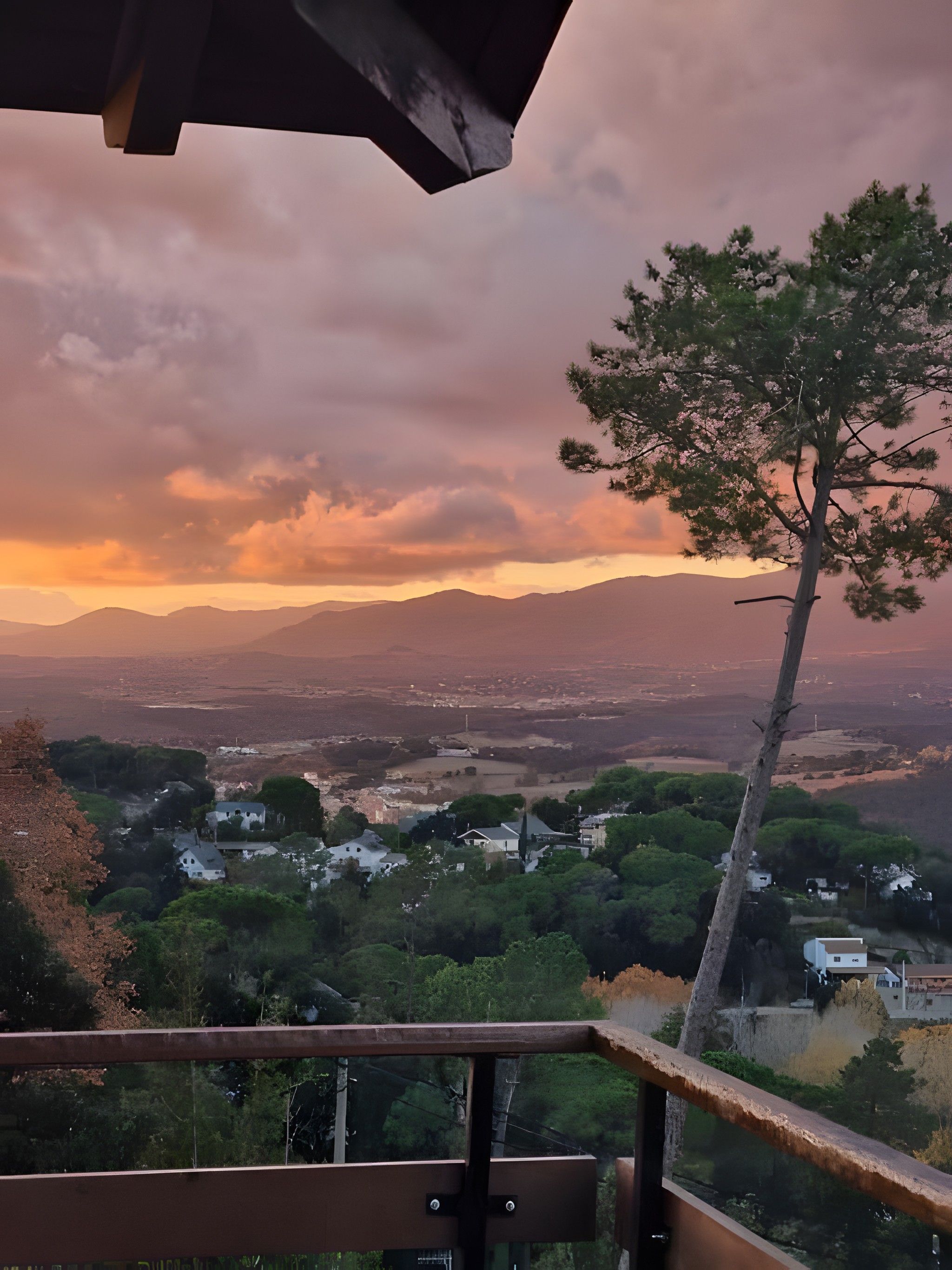A scenic view from a balcony overlooking a valley with houses and trees, under a cloudy sky.