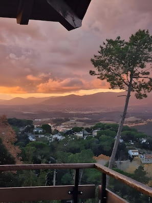 Vista panorámica desde un balcón que domina un valle con casas y árboles, bajo un cielo nublado.