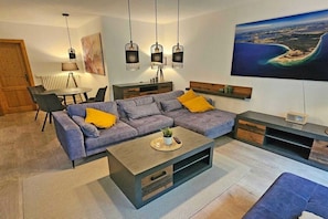 Uma sala de estar moderna com um sofá modular, uma mesa de centro e uma área de jantar com mesa e cadeiras.