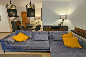 A modern living room with a sectional sofa, a dining table, and pendant lighting. - Holiday apartment with 1 bedroom (Prerow)