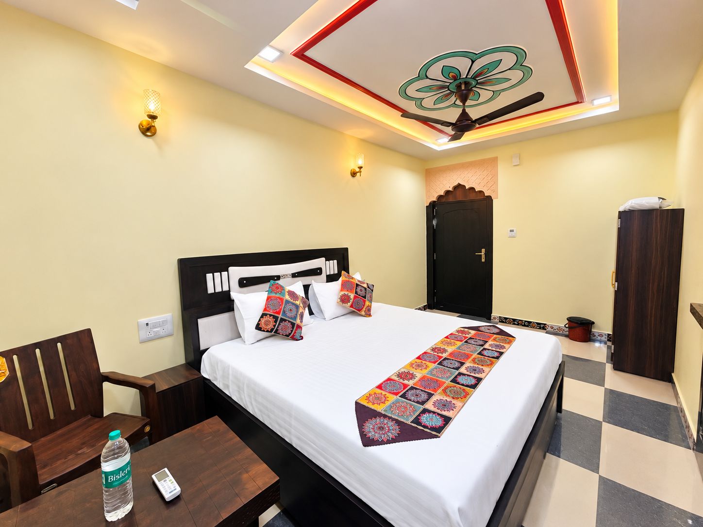 A hotel room with a bed, bedside table, chair, wardrobe, and a ceiling fan.