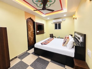 A hotel room with a bed, a ceiling fan, a mounted TV, an air conditioning unit, and a checkered floor.