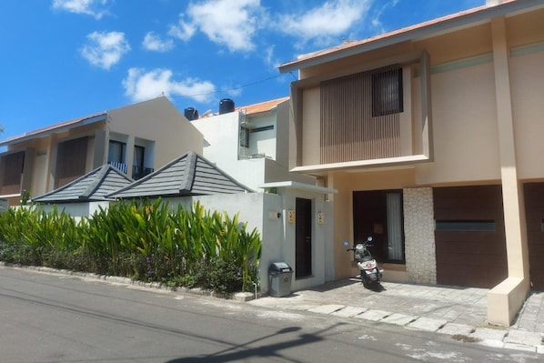 A residential street with modern houses, a parked scooter, and a clear sky.