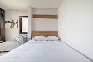 A modern hotel room with a large bed, a seating area, and a window with blinds.