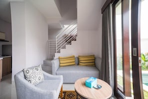 A modern living room with a grey sofa, patterned cushions, a round coffee table, and a staircase leading to an upper level.