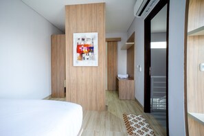 A hotel room with a bed, a wooden wardrobe, a bathroom with a towel, and a staircase leading to an outdoor area.