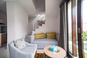 A modern living room with a grey sofa, patterned cushions, a round coffee table, and a staircase leading to an upper level.