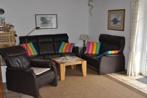 Ein Wohnzimmer mit einer schwarzen Ledersofa, zwei Sesseln, einem Holztisch und bunten Kissen.