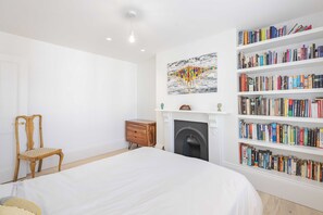 Ein Schlafzimmer mit einem großen Bett, einem Holznachttisch, einem Bücherregal, einem Kamin und einem Bild an der Wand.