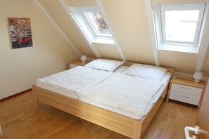 Een slaapkamer met een houten bed, twee nachtkastjes, een bijzetmeubel en een dakvenster.