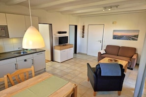 A compact living space with a kitchenette, a dining area, a seating area with a sofa and armchairs, and a door leading to another room. - Guesthouse "Wangerland" for up to 4 people (Wangerland)