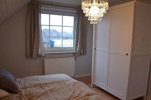 A bedroom with a bed, a window with curtains, a radiator, and a wardrobe. - Holiday home Lieselotte (Hooksiel)