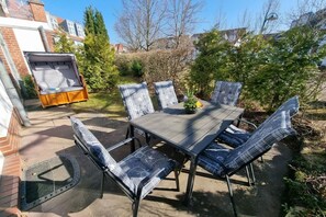 Eine Terrasse im Freien mit Esstisch und Stühlen, einer gepolsterten Bank und einer Fußmatte.