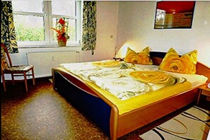 Ein Schlafzimmer mit einem Bett, einem Sessel, einem Fenster mit Vorhängen und einer Heizung.