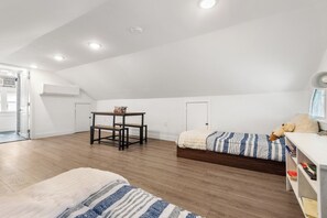 Ein geräumiger Raum mit schrägem Dach, einem Holztisch, zwei Betten und einem weißen Klimagerät.