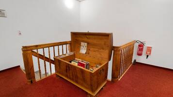 Un cofre de madera con libros en su interior, ubicado en una habitación con alfombra roja y baranda de madera.